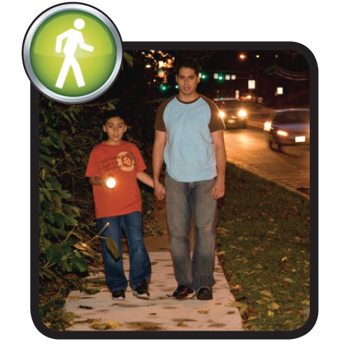 Two people walking on the sidewalk at night with a flashlight