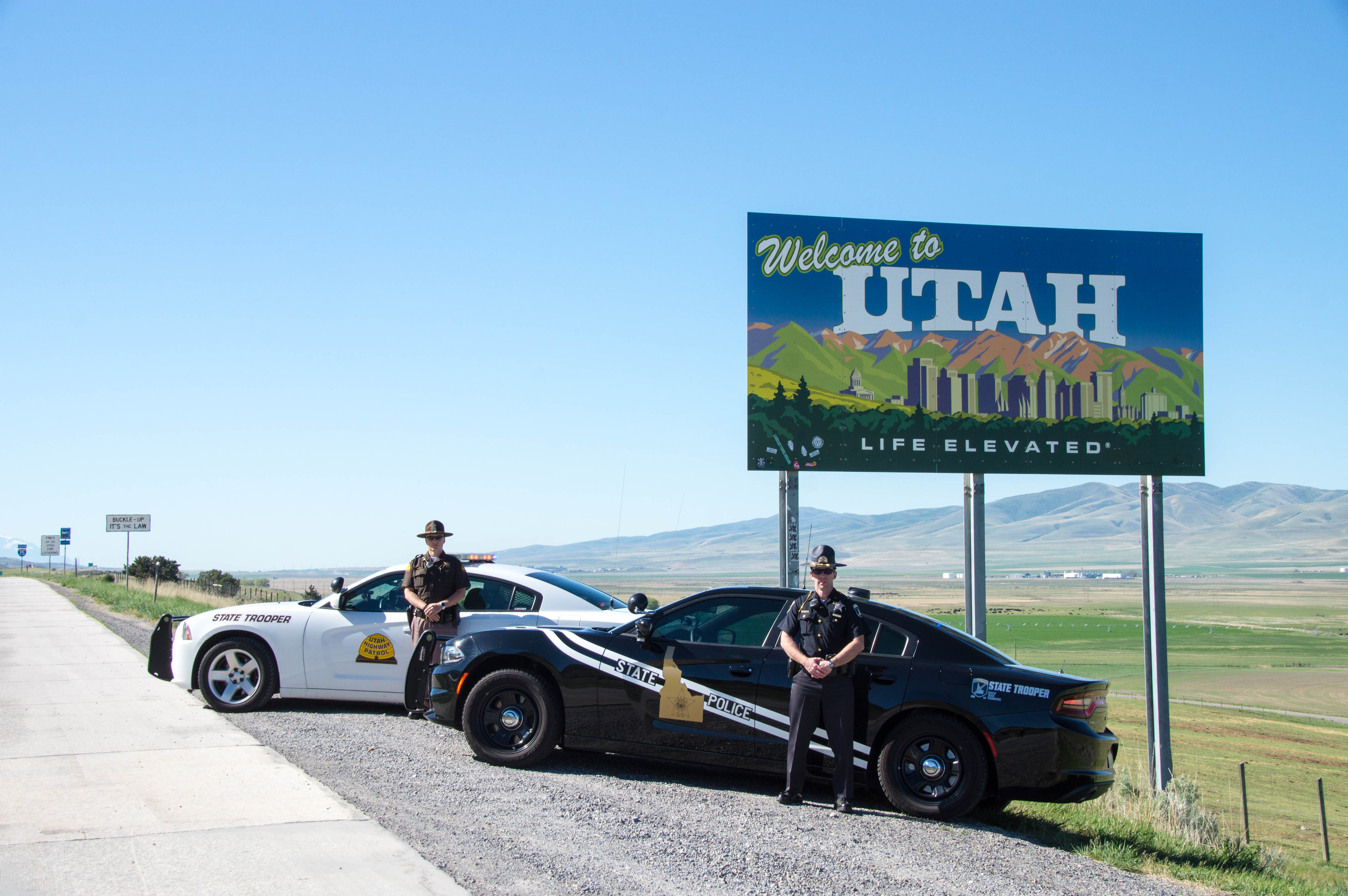 A UHP Trooper and ISP Trooper stand by their vehicles at the "Welcome to Utah" Sign
