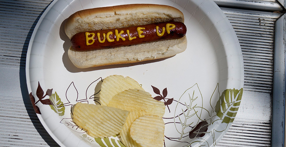 Hot dog with buckle up written in mustard on it.