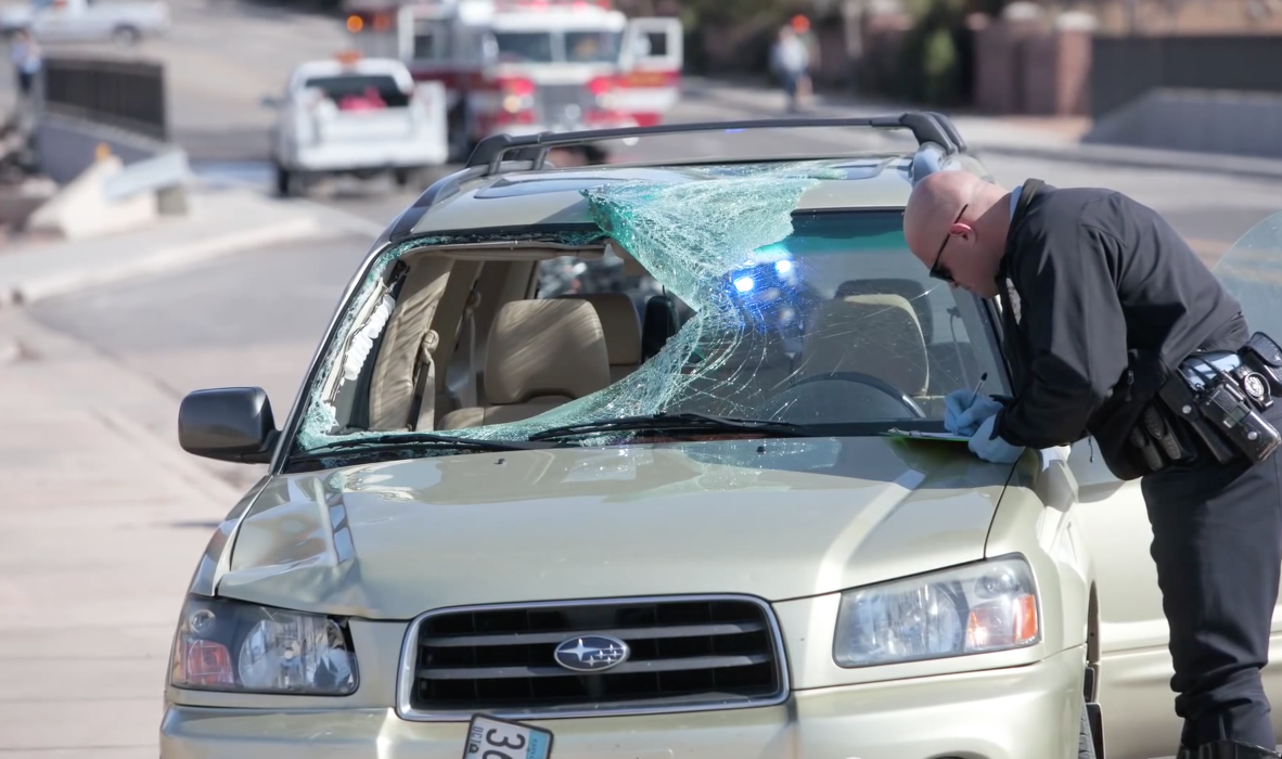 St. George PD filling out paper work on hood of car with windshield smashed in from fatal crash caused by distracted driver