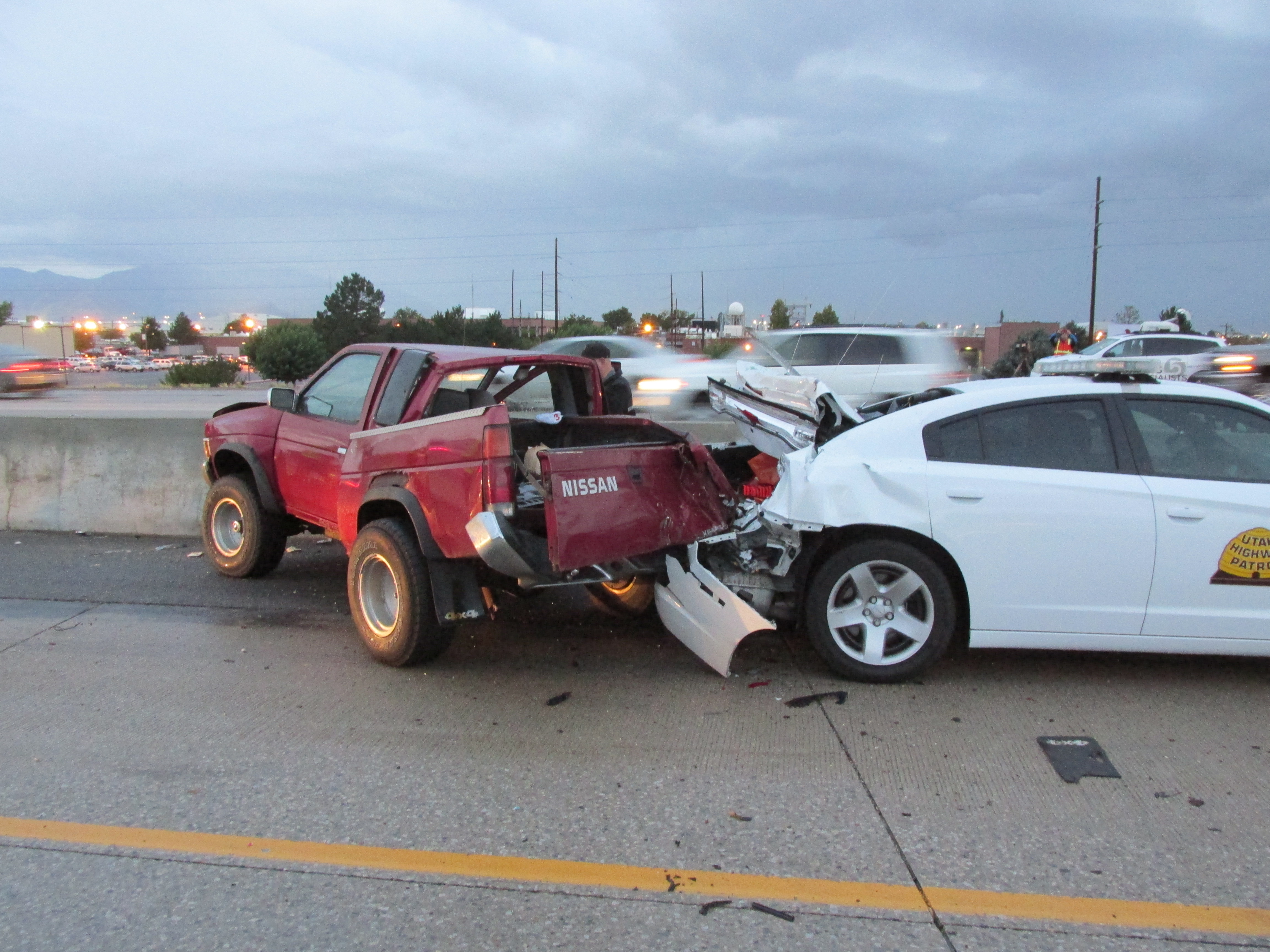 A UHP trooper's vehicle received significant damage when a car crashed into it on the road shoulder.