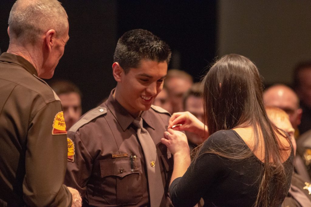 Trooper has his badge pinned on him by his spouse.