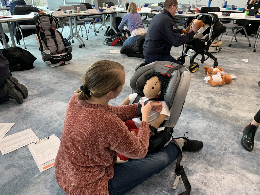 A CPS class students works to properly fit car seat straps around a mannequin.